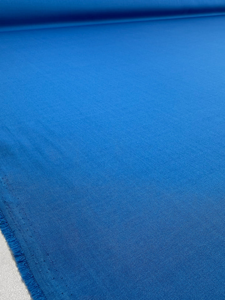 A close-up of Super Cheap Fabrics’ Liquid Twill - French Blue - 150cm spread out, showcasing its texture and smooth finish.