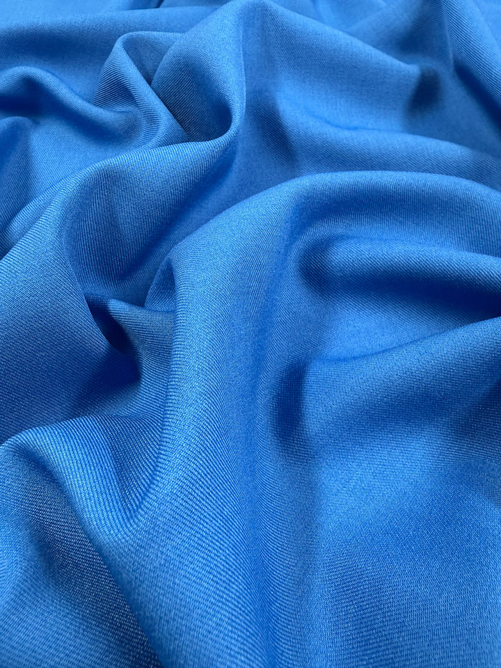 A close-up of Super Cheap Fabrics' Liquid Twill - French Blue - 150cm shows soft folds and gentle wrinkles, highlighting its vibrant color and smooth, textured finish.
