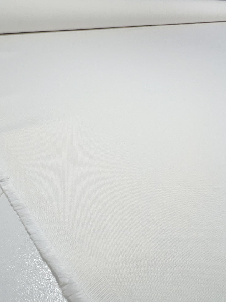 A close-up of Super Cheap Fabrics' Slubbed Linen Drill in Vanilla, 140cm wide, shows its subtle texture and smooth appearance. The fabric's edges are slightly frayed against a soft, neutral background.