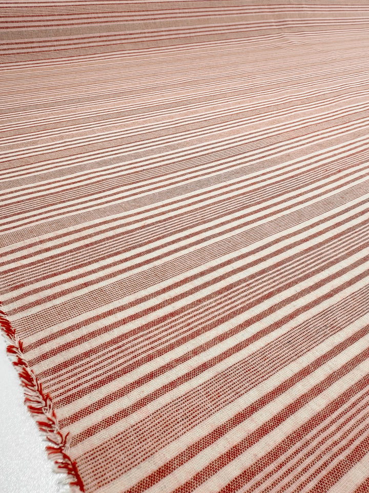 A close-up of Super Cheap Fabrics' Linen Blend - Rosebay Stripe (145cm) shows lightweight linen fabric with red and white horizontal stripes of varying thicknesses and a slightly frayed edge on the left side.