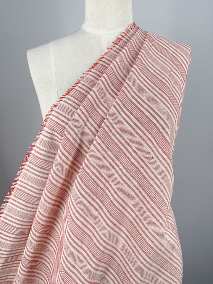 A white dress form displays Super Cheap Fabrics’ Linen Blend - Rosebay Stripe (145cm), a lightweight fabric with thin red and white horizontal stripes and a fringed edge, against a plain gray background.