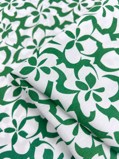 A close-up of the Designer Rayon - Green Bee by Super Cheap Fabrics showcases a 140cm versatile fabric with a green and white floral pattern, featuring overlapping flowers with bold green outlines on a white background for striking projects.