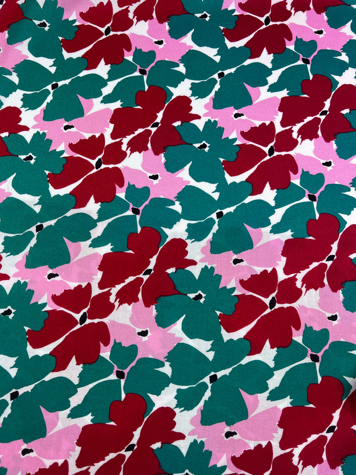 The Designer Rayon - Spring by Super Cheap Fabrics features a vibrant floral pattern with abstract red, green, and white shapes on a pink background. This 140cm fabric offers bold designs that create lively and dynamic visuals.