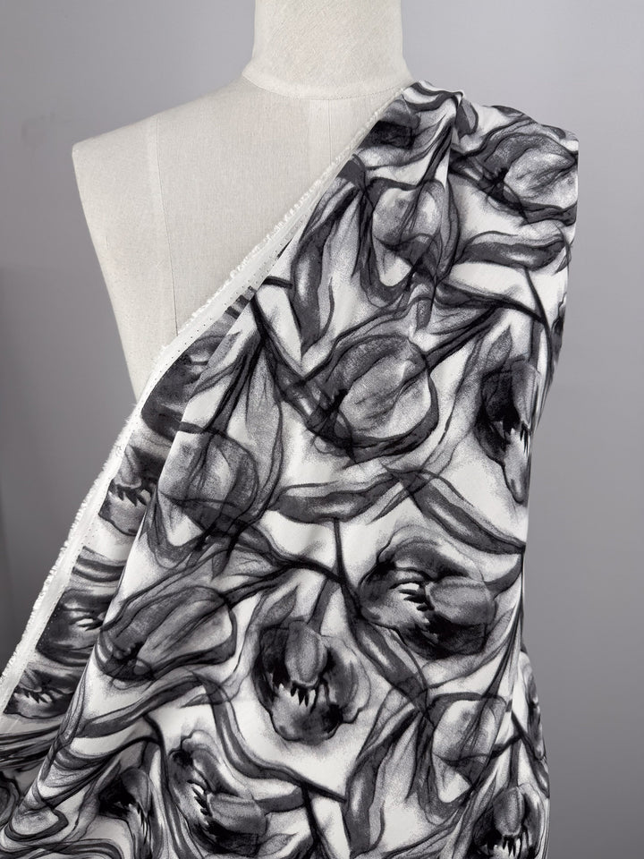 A white mannequin is draped in Super Cheap Fabrics' Designer Rayon - Shadow Petal (148cm), showcasing its lightweight, black-and-white abstract tulip floral pattern flowing diagonally across the chest.