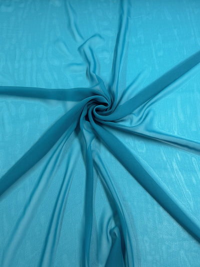 A swirling arrangement of Hi-Multi Chiffon - Horizon Blue - 150cm from Super Cheap Fabrics is displayed, creating a spiral pattern in the center. The lightweight fabric appears translucent and smooth, with soft folds radiating outward from the center twist.