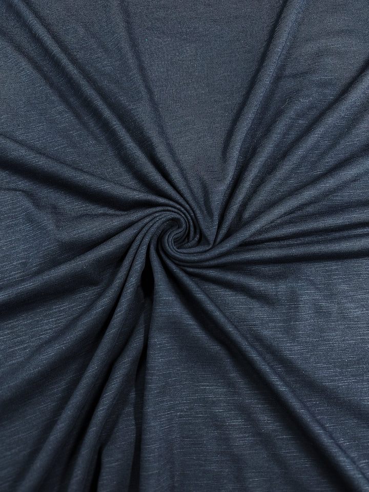 A close-up of a dark blue or navy Bamboo Jersey - Navy - 150cm from Super Cheap Fabrics with a slight sheen, gathered and spiraled at the center to create a swirling pattern. The texture appears smooth and soft, reflecting its environmentally responsible origins.