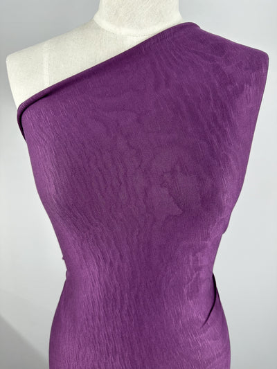 A dress form draped in a purple, one-shoulder garment made from Bamboo Jersey - Deep Purple - 150cm by Super Cheap Fabrics. The textile has a slightly textured appearance, giving it a light sheen. The background is plain and neutral, focusing attention on the environmentally responsible garment.