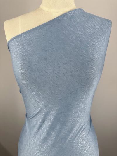 A Super Cheap Fabrics Bamboo Jersey - Powder Blue - 150cm dress crafted from bamboo fabric is displayed on a mannequin. The fabric has a subtle textured pattern and a soft to medium sheen. The dress contours smoothly, highlighting its elegant and minimalist design. The background is a plain, neutral shade.