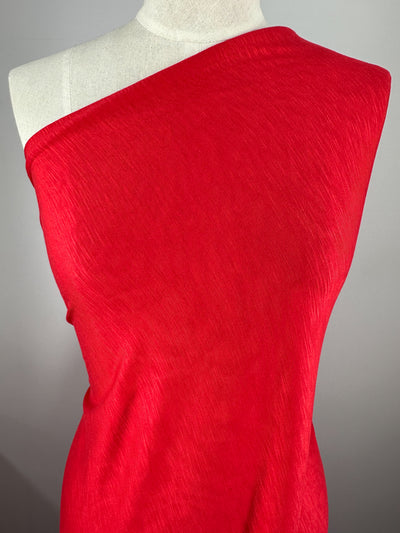 A close-up view of a red, off-the-shoulder garment displayed on a mannequin against a plain, light gray background. Made from environmentally responsible bamboo fabric, the semi-sheer material drapes elegantly over the form of the mannequin and is silky to the touch. The garment features Bamboo Jersey - Scarlet Red - 145cm by Super Cheap Fabrics.