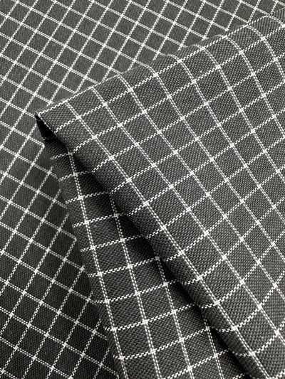 A close-up of two pieces of dark gray woven fabric with a white grid pattern. Perfect for home decor items, the fabric pieces are layered, with one piece laid diagonally over the other, showcasing the texture and design of the Linen Rayon Grid - Charcoal - 145cm from Super Cheap Fabrics.
