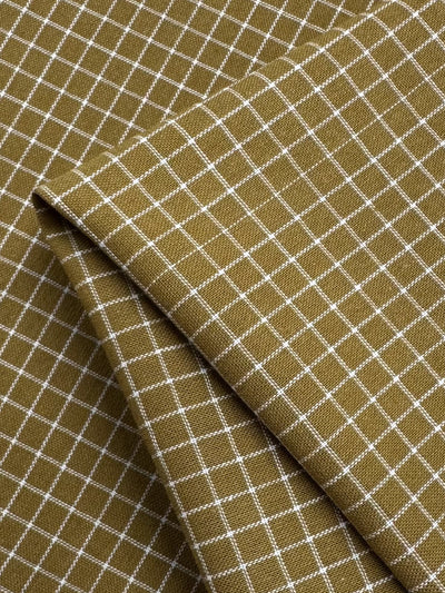 Close-up of Linen Rayon Grid - Mustard - 145cm by Super Cheap Fabrics featuring a grid pattern of white lines. The fabric is folded over itself, creating multiple layers and showcasing the intricate designs and texture, perfect for home decor.