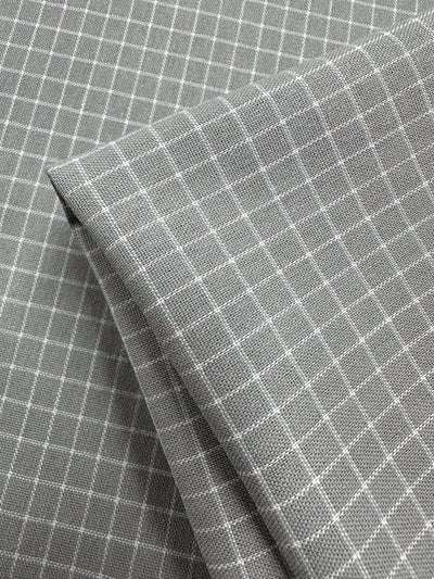 A close-up image of gray fabric with a white grid pattern. The high-quality Super Cheap Fabrics Linen Rayon Grid - Grey - 145cm is neatly folded, showcasing the intersecting lines that form small squares across the material. This versatile material features a smooth, finely woven texture, ideal for various home decor items.