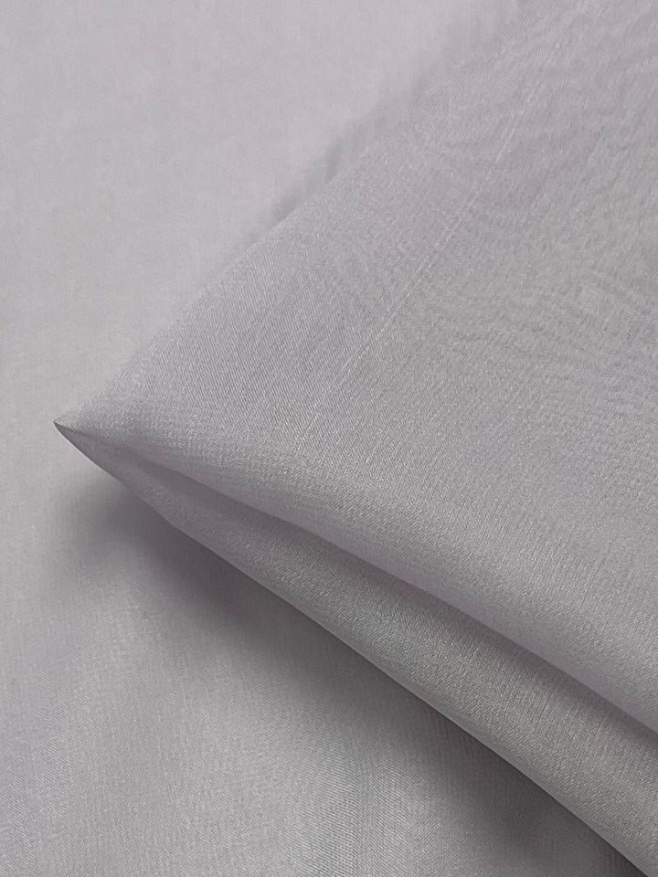 A close-up view of a neatly folded piece of light grey fabric reveals a smooth and slightly shiny texture. The Silk Georgette - Orkid - 135cm by Super Cheap Fabrics appears soft and lightweight, making it perfect for summer outfits.