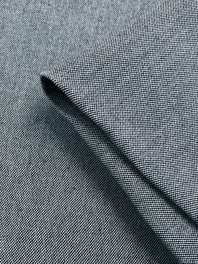 Close-up image of a folded piece of Canvas - Pageant Blue - 150cm from Super Cheap Fabrics with a fine, textured weave pattern. The material appears smooth and neatly pressed, showcasing a subtle, elegant texture. The fold creates a slight shadow, enhancing the depth and detail of the upholstery fabric.
