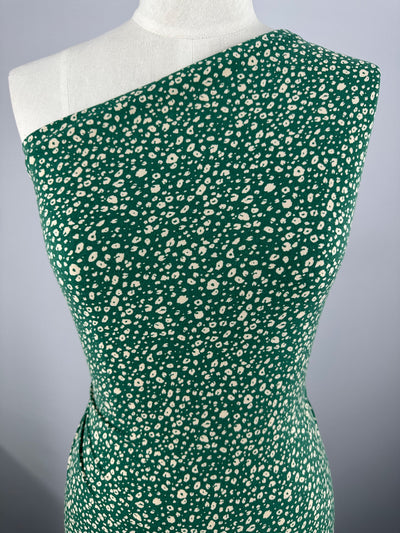 A green Printed Lycra - Dotty Green - 150cm adorned with a pattern of small white flowers is displayed on a dress form. Made by Super Cheap Fabrics from medium-weight fabric, the charming piece stands out against the solid, light gray background.