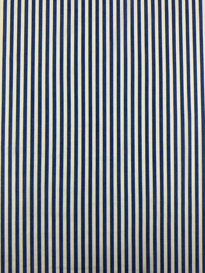 A pattern of vertical blue and white stripes evenly spaced across the entire image. The stripes are parallel and consistently aligned, creating a uniform design reminiscent of lightweight fabric used in clothing. The background alternates between blue and white lines, showcasing the Cotton Lawn - Blue Stripe - 150cm by Super Cheap Fabrics.