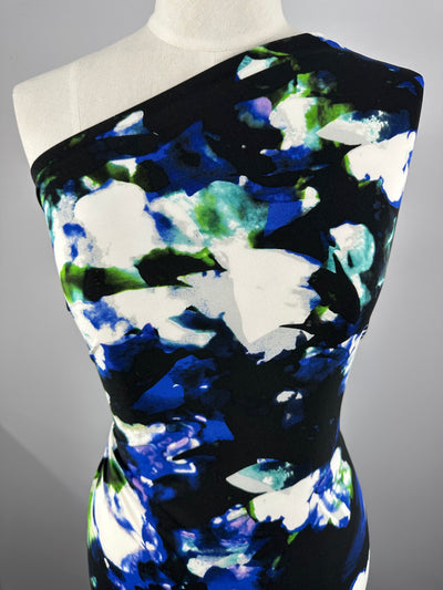 A close-up of a Printed Lycra - Moon Mist - 150cm from Super Cheap Fabrics on a mannequin, featuring an abstract floral pattern in shades of blue, green, white, and black. Made from polyester spandex, the medium-weight fabric offers a fitted silhouette and smooth texture against a plain gray background.