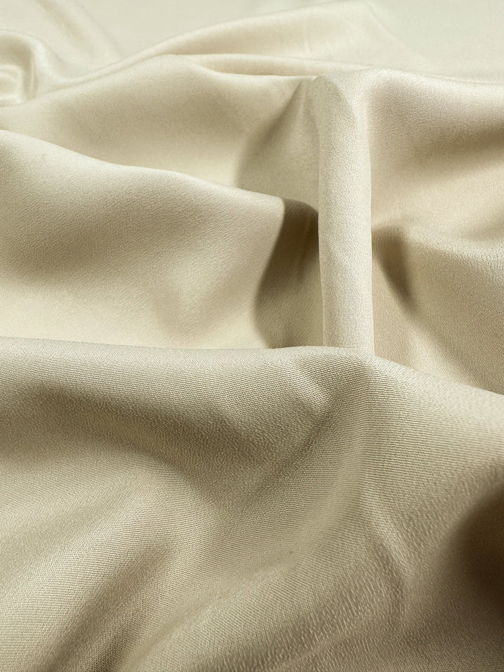 A close-up of a piece of Super Cheap Fabrics' Microfibre - Oat - 150cm fabric with a smooth, soft texture. The lightweight material has gentle folds and a slight sheen, creating subtle shadows and highlights across the surface.
