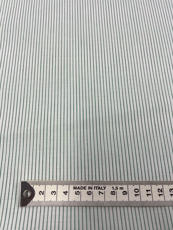 The Shirting - Harp - 145cm by Super Cheap Fabrics is a close-up of lightweight polyester cotton fabric featuring thin vertical green and white stripes. A measuring tape indicating centimeters is laid across the bottom, stamped with "MADE IN ITALY." This versatile material is ideal for various projects.