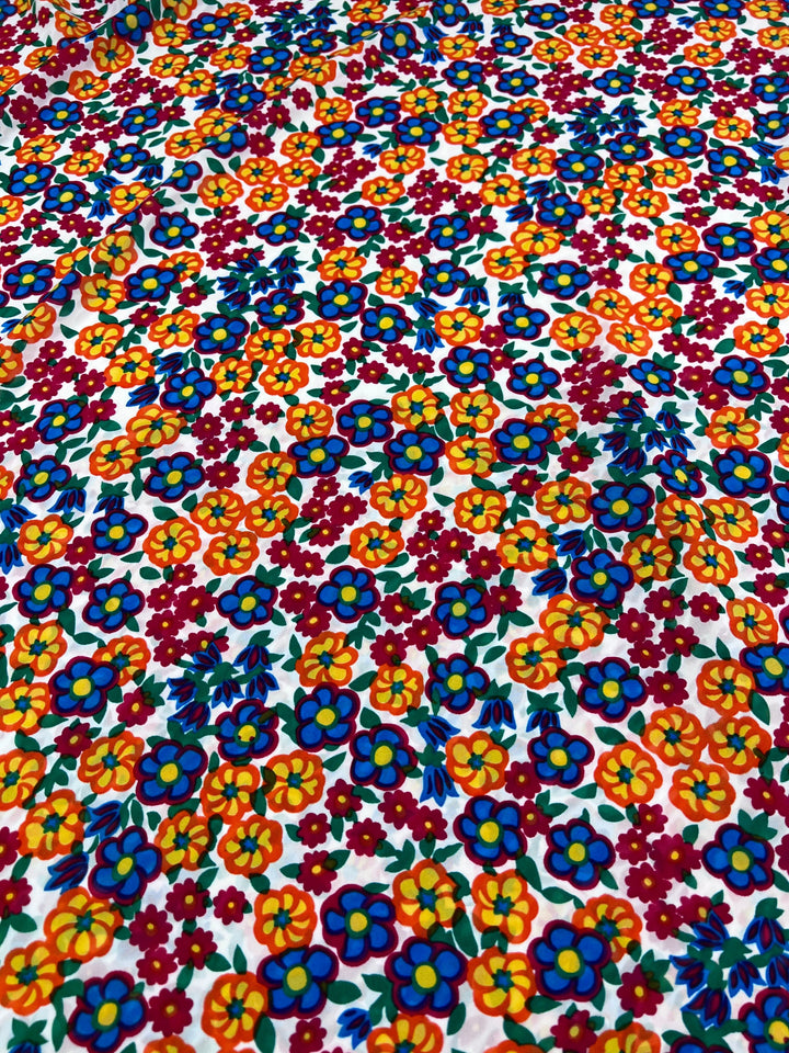 The Salt Shrunk Print - Pansy by Super Cheap Fabrics features a vibrant floral design with dense orange, blue, red, and yellow flowers on a white backdrop for an elegantly colorful look.