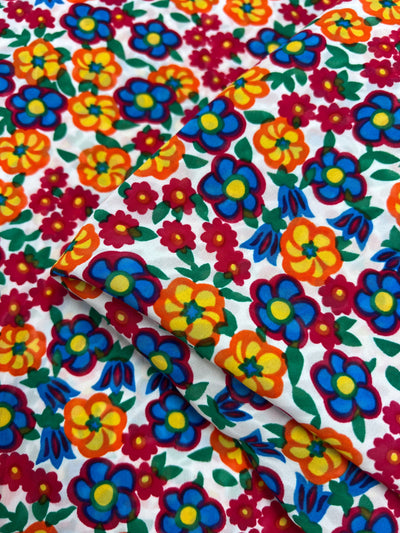 The Salt Shrunk Print - Pansy by Super Cheap Fabrics is a vibrant, elegant fabric featuring a dense floral pattern of red, yellow, blue, and orange flowers with green leaves on white.