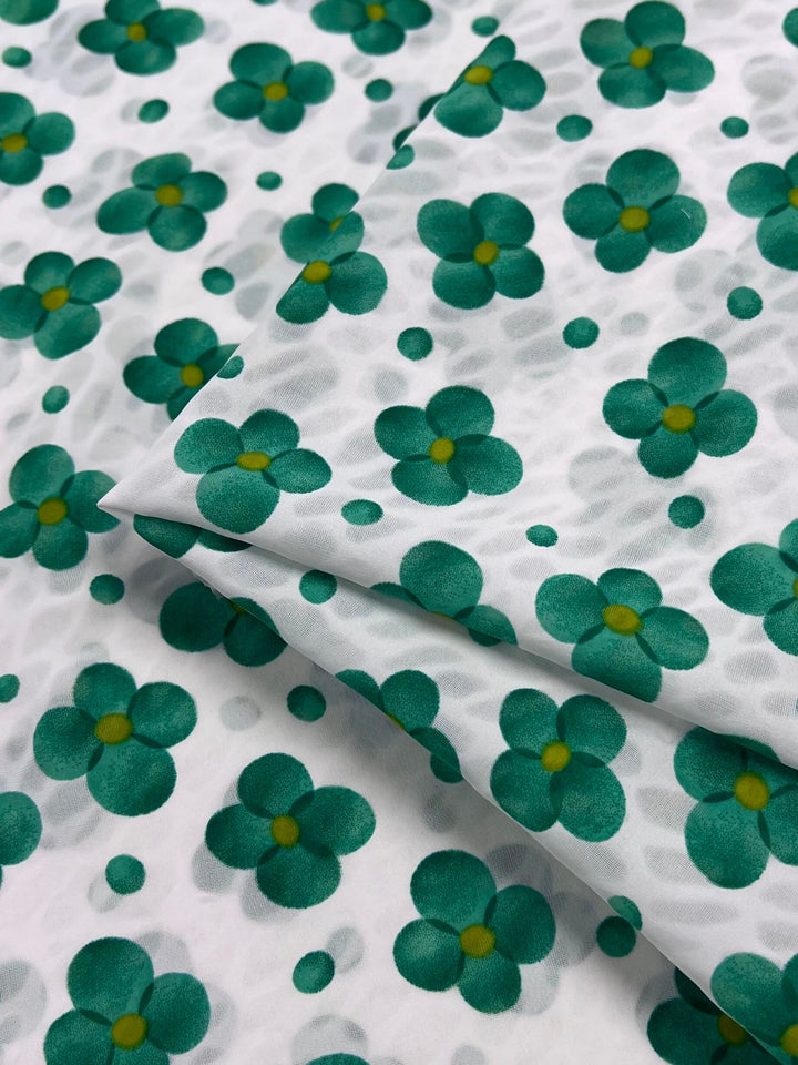 The Salt Shrunk Print - Clover by Super Cheap Fabrics is a 155cm white fabric adorned with green four-petaled flowers and small dots. Vibrantly colored, it is perfectly folded to highlight its unique design, making it a standout in any collection.