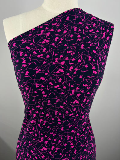 A mannequin is draped with Super Cheap Fabrics' Printed Lycra - Barbwire Heart - 150cm, featuring a vivid pink heart and vine pattern, creating a striking contrast and dynamic, feminine design. The fabric tightly fits the mannequin, highlighting its contours.