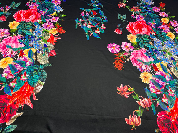 A vibrant, intricate floral pattern featuring an array of colorful flowers and green foliage set against a black background. Made from a nylon spandex blend with 2-way stretch, the multi-use fabric showcases roses, lilies, and various other species, creating a striking and dynamic visual composition. Introducing the Floral Scuba - 170cm Panel by Super Cheap Fabrics.