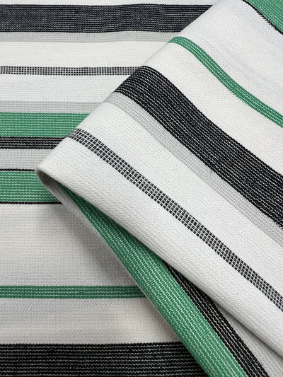 Close-up of a folded fabric from the Designer Cotton - Green Rock Candy - 145cm by Super Cheap Fabrics with a woven pattern consisting of horizontal stripes in white, black, grey, and green. The sustainable deadstock material has a slightly textured appearance, with evenly spaced and uniformly sized stripes.