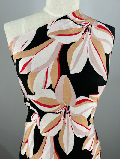 A mannequin is draped with a light-medium weight fabric, featuring a bold floral pattern with large white, beige, pink, and red flowers. This versatile fabric is displayed against a neutral gray background. The product used is the Printed Rayon Lycra - Lily - 150cm from Super Cheap Fabrics.
