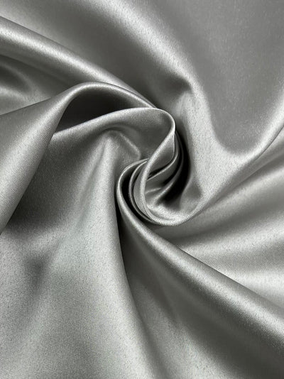 A close-up of smooth, shiny **Delustered Satin - Vaporous Gray - 150cm** fabric with a swirling fold in the center, showcasing its silky texture and delicate sheen from **Super Cheap Fabrics**.