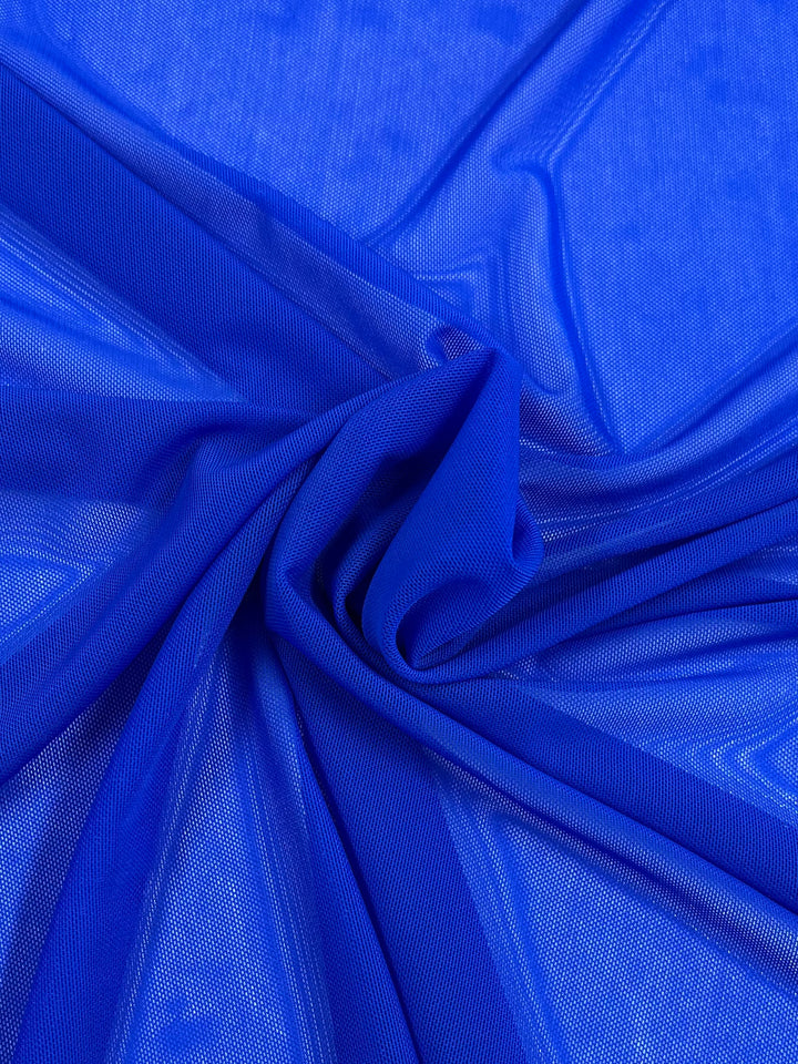 A close-up of Super Cheap Fabrics' Plain Mesh - Dazzling Blue (155cm) shows vivid blue polyester with a mesh-like texture, gently gathered into folds. It's lightweight and semi-sheer, ideal for clothing or decor.