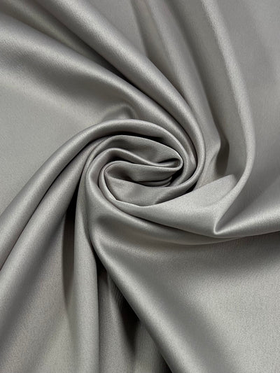 Close-up image of Super Cheap Fabrics' Delustered Satin - Oyster Grey - 150cm, neatly arranged in a swirling pattern that showcases its smooth and shiny texture. This medium weight, 100% polyester material's folds and drapes create a sense of elegance and softness.