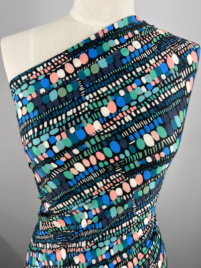 A close-up of a mannequin wearing Super Cheap Fabrics' Printed Lycra - Romina - 150cm, a one-shoulder garment made from medium weight fabric with a colorful abstract pattern. The polyester spandex material features various shapes including circles, rectangles, and dots in blue, green, pink, white, and black on a black background.