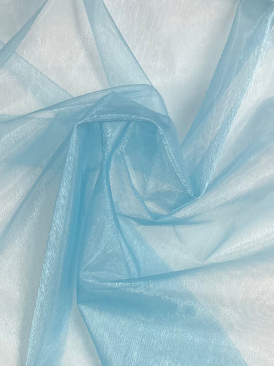 A close-up view of sky blue, extra lightweight sheer fabric with a soft, delicate texture. Made from 100% nylon, the fabric is slightly crumpled, creating a mix of light and shadow that highlights its translucent and airy quality. Product Name: Organza - Sky Blue - 150cm by Brand Name: Super Cheap Fabrics.