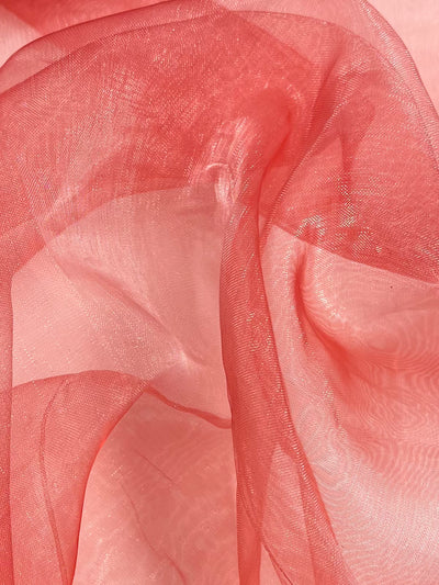 A close-up of sheer, Tea Rose and coral fabric with a delicate, almost translucent texture. The Organza - Tea Rose - 150cm by Super Cheap Fabrics is softly folded and layered, catching light to create a subtle shimmer and a sense of depth and movement.