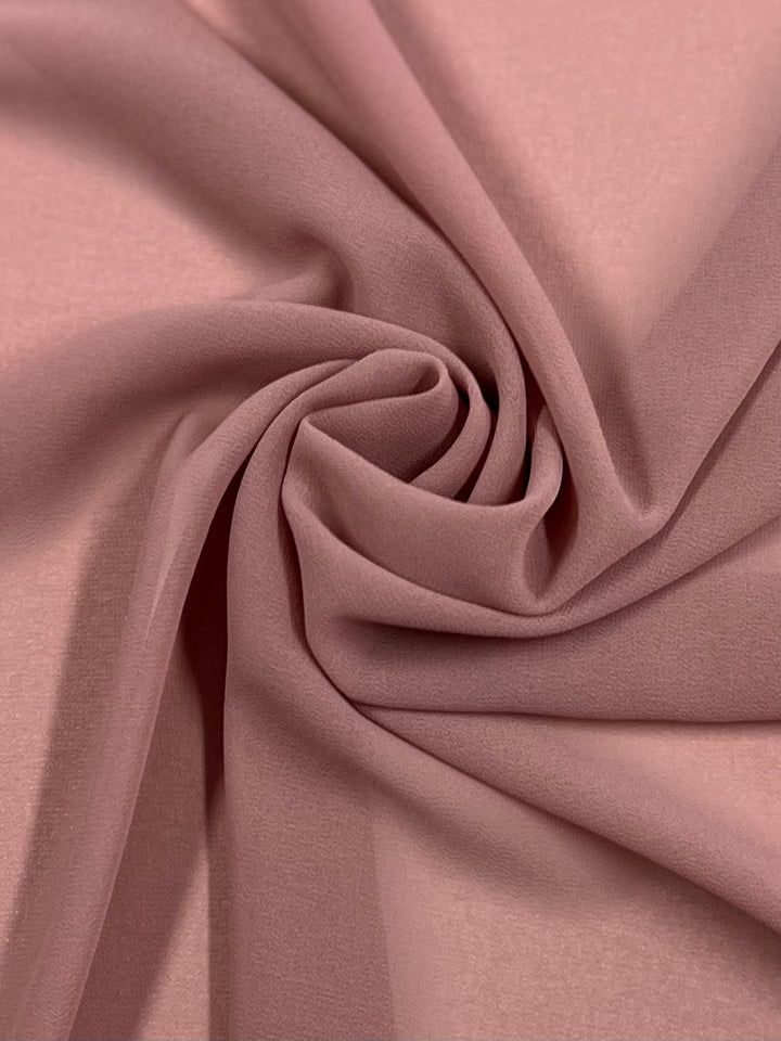 Close-up of a piece of Hi-Multi Chiffon - Rose Tan - 150cm from Super Cheap Fabrics, arranged in a twisted, swirling pattern, showcasing its smooth texture and soft folds.