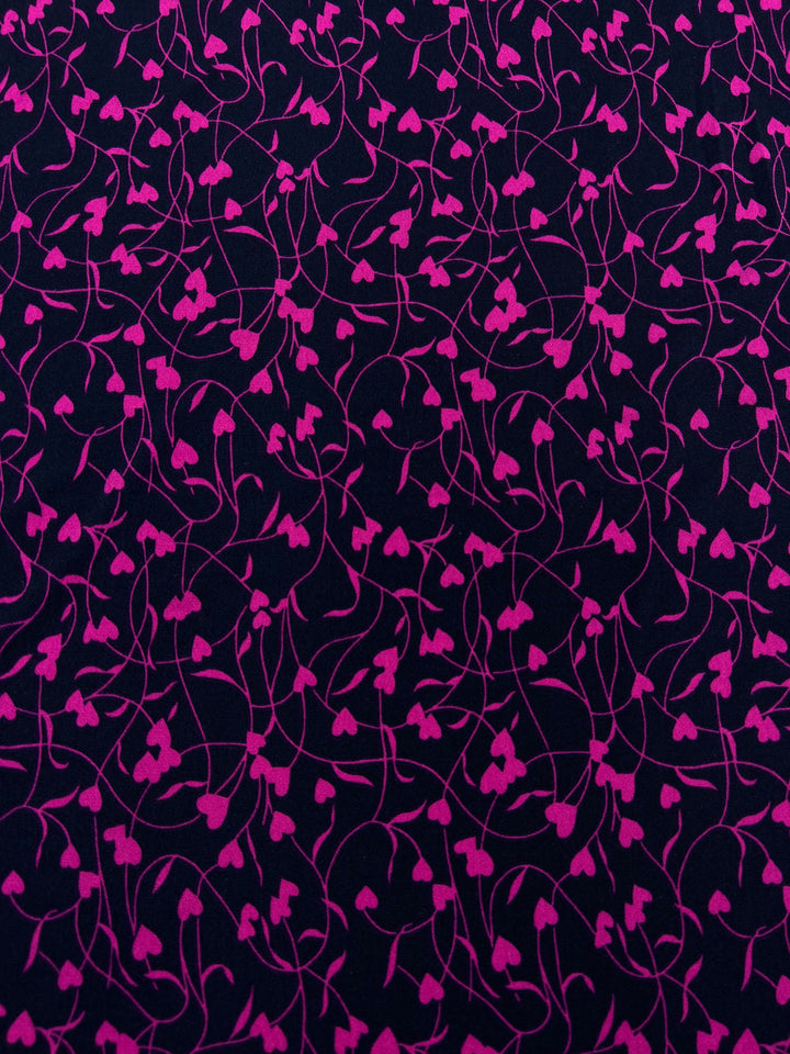 A close-up view of the Super Cheap Fabrics' Printed Lycra - Barbwire Heart - 150cm displaying an intricate pattern of navy pink vines and heart-shaped leaves on a dark purple background. The design creates a sense of movement and elegance.