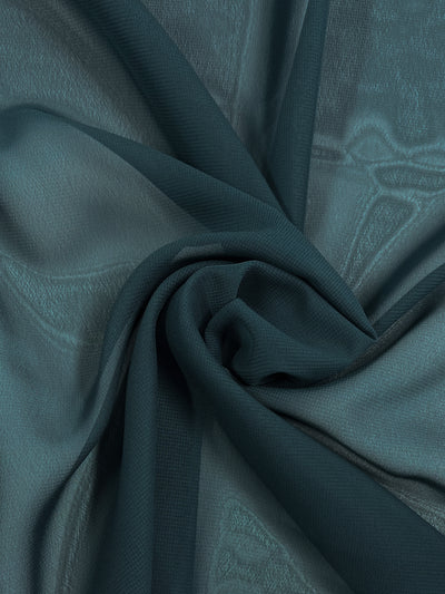 A close-up of Hi-Multi Chiffon - Dark Teal - 150cm from Super Cheap Fabrics loosely gathered in a swirl. The lightweight fabric has a light, translucent texture, revealing subtle patterns and folds. The image emphasizes the softness and fluidity of the material.
