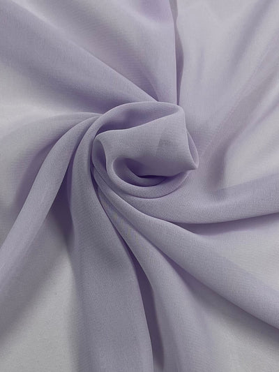 A close-up of soft, lilac fabric with a slight sheen, arranged in a swirling, circular pattern on a flat surface. The delicate folds create subtle shadows and highlights, adding texture to the image. This Hi-Multi Chiffon - Lilac - 150cm from Super Cheap Fabrics drapes elegantly, enhancing its graceful appearance.