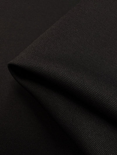 Close-up of folded black Ponte - French Toast knit fabric from Super Cheap Fabrics, showcasing its smooth texture and fine weave. The fabric exhibits a slight gloss, with subtle highlights where the light hits it. The folded edge creates a gentle shadow, adding depth to the image.