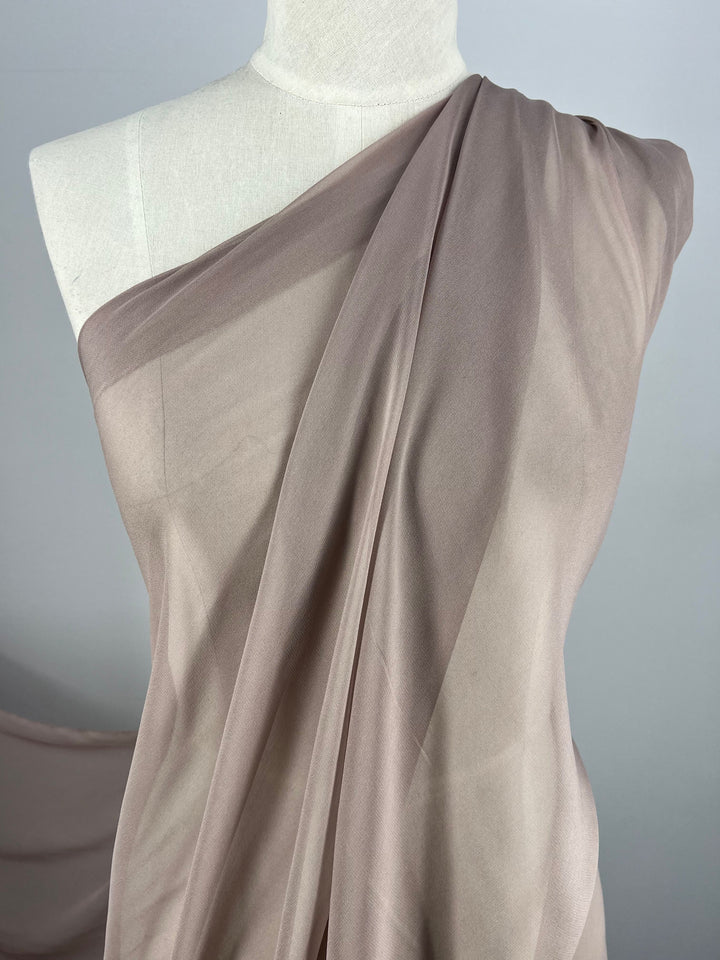 A beige Silk Georgette - Quail fabric from Super Cheap Fabrics, draped elegantly over a white dress form, showcases its soft, flowing texture and subtle sheen. The 135cm wide sheer plain silk georgette is arranged to reveal delicate folds and gentle curves, highlighting its lightweight and translucent qualities—perfect for summer outfits.