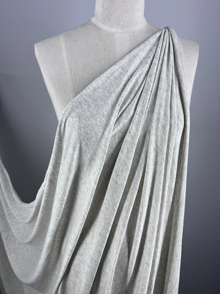 The Summer Cotton Knit - Grey Marle by Super Cheap Fabrics drapes elegantly on a mannequin, revealing smooth folds, a soft texture, and impressive stretch for a sophisticated, fluid design.