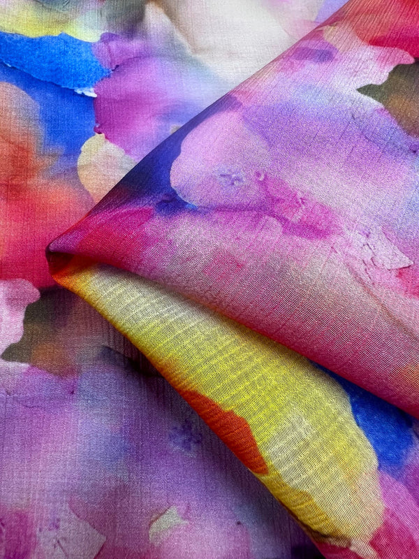 A close-up of the Super Cheap Fabrics Designer Cotton - Wonder - 150cm reveals a colorful abstract watercolor pattern. Vibrant pinks, purples, blues, yellows, and oranges blend seamlessly for a soft artistic effect. Perfect for luxury sewing projects, the fabric is folded diagonally.