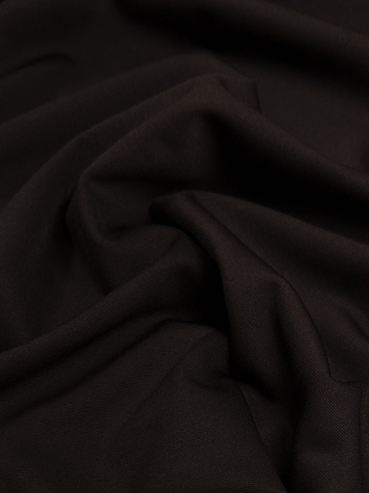 A close-up of "Ponte - French Toast - 155cm" by Super Cheap Fabrics, showcasing the black heavyweight ponte fabric with soft folds and drapes that create subtle shadows and highlights on its smooth, slightly matte surface.