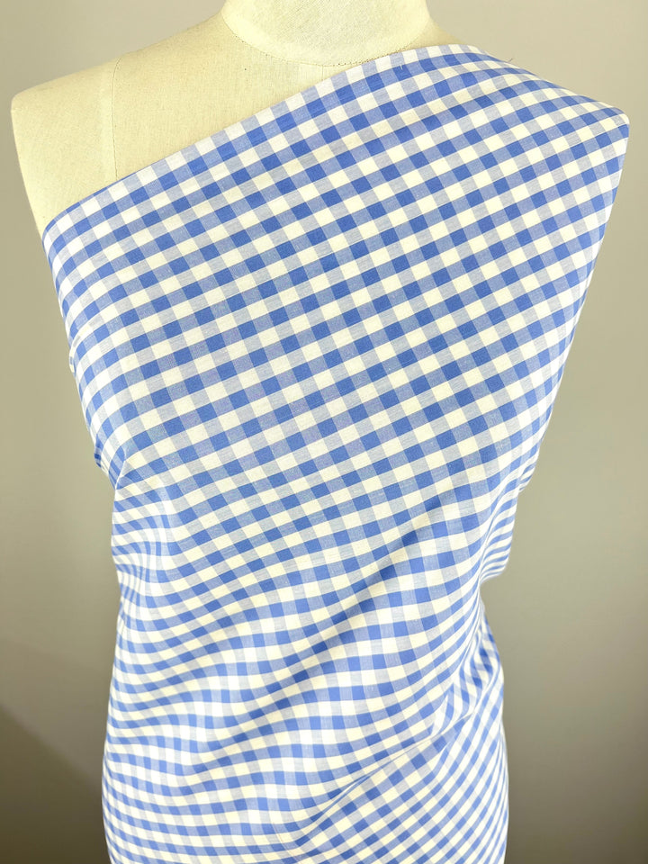 A dressmaker's mannequin draped with *Cotton - Frozen Gingham - 145cm* from *Super Cheap Fabrics*. The lightweight 100% cotton fabric is arranged diagonally across the chest, showcasing the classic checkered pattern. The background is a neutral light grey, drawing attention to the fabric's details.