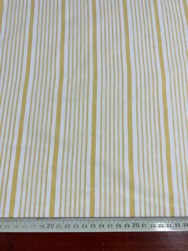 A piece of Cotton Voile - Popcorn Stripe - 150cm from Super Cheap Fabrics with vertical yellow and white stripes lies on a flat surface. A ruler at the bottom of the image measures 40 centimeters, providing a sense of scale. The silky finish suggests it could be ideal for warm weather clothing. The background appears to be a wooden table.