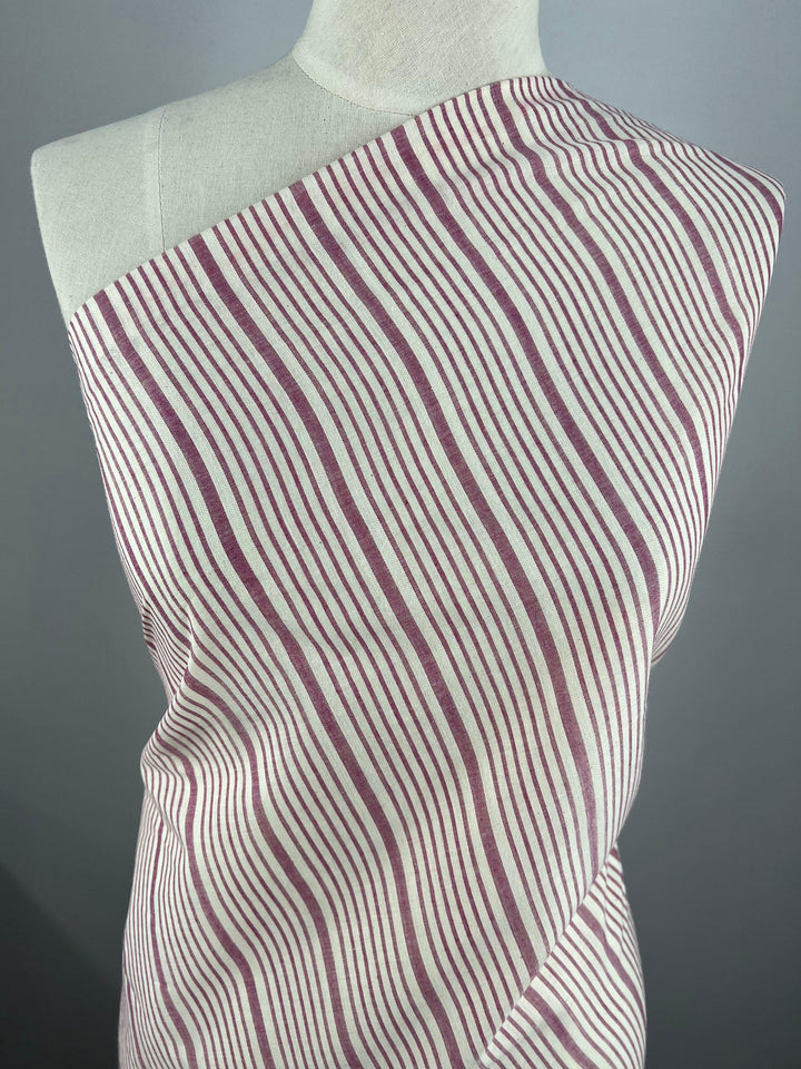 Close-up of a white dress form draped with Super Cheap Fabrics' Cotton Voile - Magenta - 150cm fabric featuring vertical wavy lines in a burgundy and white striped pattern. The design creates a visually dynamic effect against the plain background, highlighting the lightweight fabric's elegance.