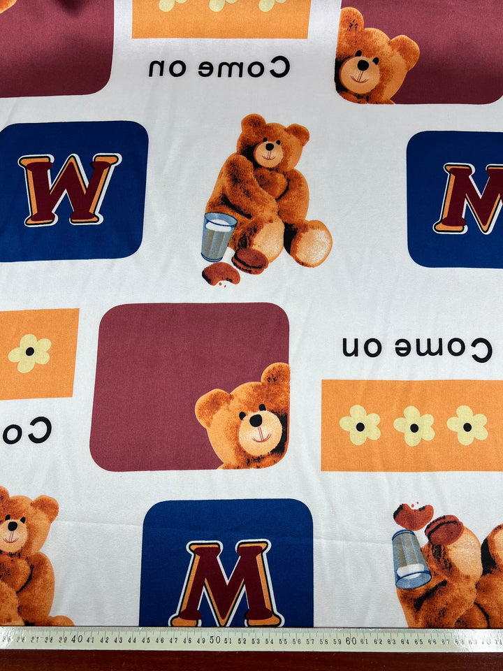 A vibrant and playful patterned fabric featuring teddy bears holding salt or sugar shakers, the letter "M" in bold red within blue and yellow rectangles, "Come on" text in black, and yellow flower shapes on a white background. The Super Cheap Fabrics Printed Satin - Playtime - 150cm is crafted from 100% polyester for an elegant touch.