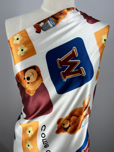 Close-up of luxurious Printed Satin - Playtime - 150cm by Super Cheap Fabrics with a playful design draped over a dress form. The 100% polyester fabric features illustrations of teddy bears, yellow flowers, and colorful squares with letters, such as "W," in a mix of blue, red, and orange.